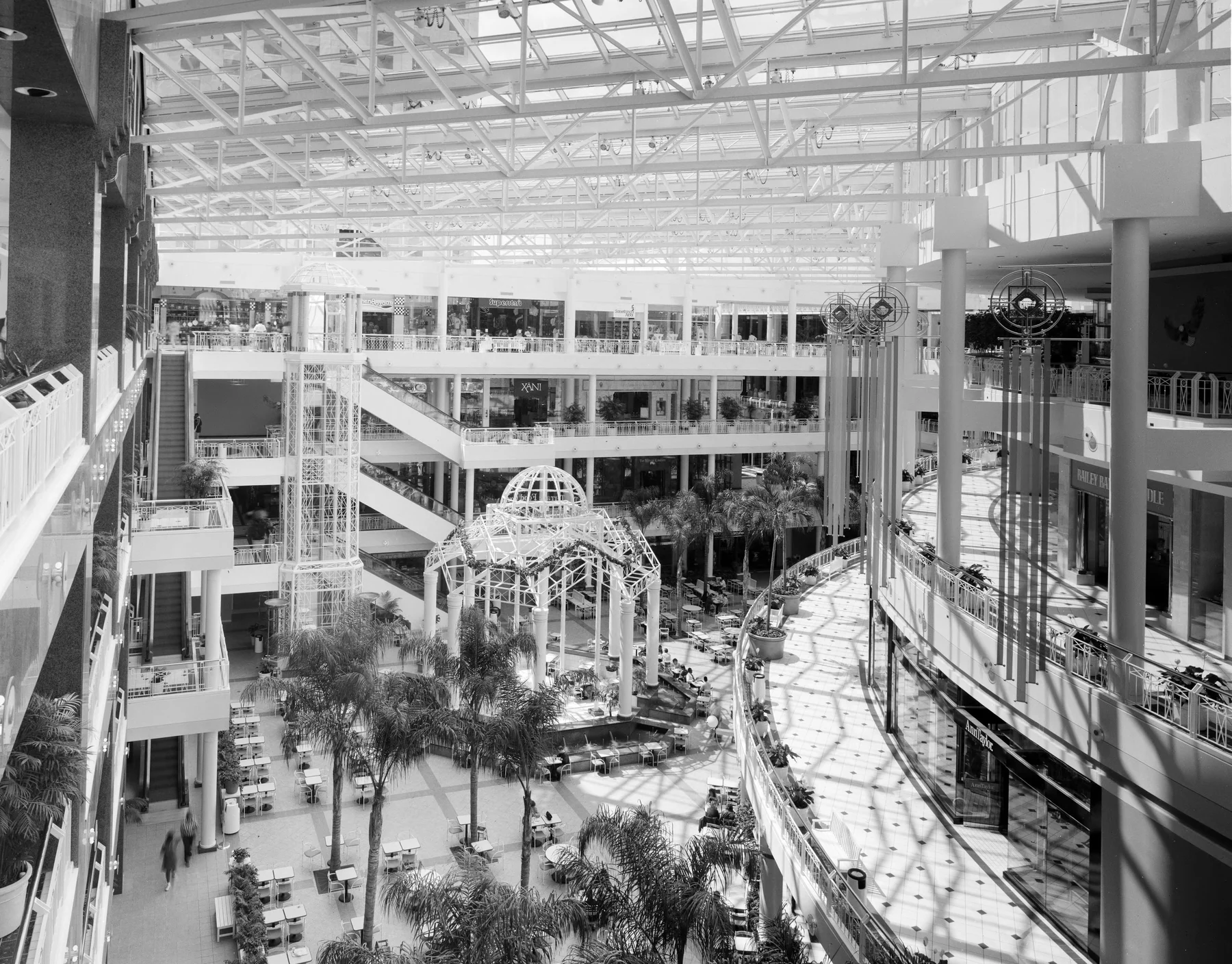 The glass-roofed atrium of the Fashion Centre at Pentagon City in Arlington, Virginia, with palm trees, tiered balconies, escalators and a food court, almost empty of people