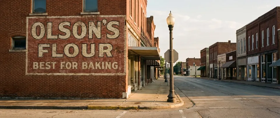 Ghost sign reading Olson's Flour, a faded hand-painted advertisement on a brick building on an American Main Street at golden hour