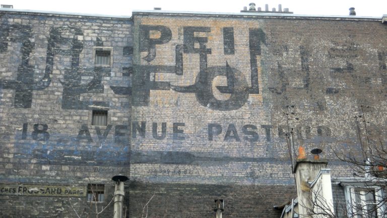 A palimpsest ghost sign on a Paris firewall: overlapping painted advertisements including the words 18 Avenue Pasteur and two billposting contractors' marks
